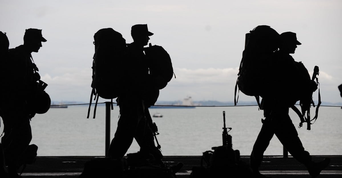 Silhouettes of military personnel walking in front of water
